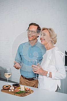 happy senior couple drinking wine and looking away while eating delicious snacks