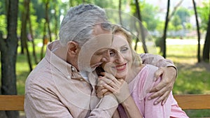 Happy senior couple embraces in park, man hugging woman, love until old age