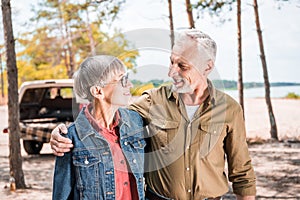 happy senior couple embracing and looking at each other in forest in sunny day.