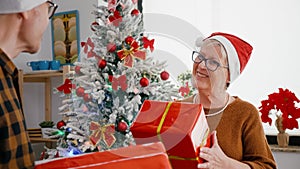 Happy senior couple enjoying christmastime sharing wrapper gift present in xmas decorated kitchen