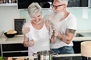 Happy senior couple enjoying and cooking healthy dinner together at home - Focus on faces