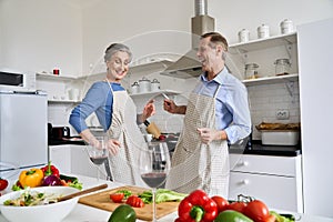 Happy senior couple enjoying dancing and cooking healthy meal together at home.
