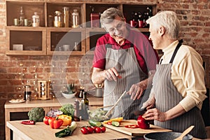 Happy senior couple enjoying preparing dinner together, cooking in kitchen