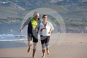 Happy senior couple enjoying running barefoot on sand near sea