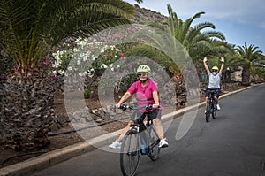 Happy senior couple enjoys sport activity with electric bikes, fun retirement concept. Palm trees and flowers in the background