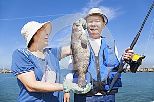 Happy senior couple fishing and showing big grouper photo