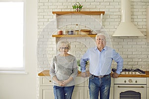 Happy senior couple grandparents standing and looking at camera together in kitchen