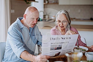 Happy senior couple having breakfast and reading newspaper together at home.