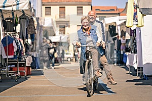 Happy senior couple having fun with bicycle at flea market