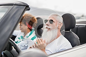 Happy senior couple having fun in convertible car during summer vacation - Focus on senior man face