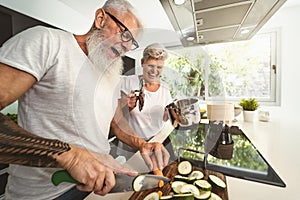 Happy senior couple having fun cooking together at home - Elderly people preparing health lunch in modern kitchen