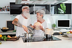 Happy senior couple having fun cooking together at home - Elderly people preparing health lunch in modern kitchen