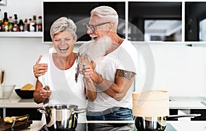 Happy senior couple having fun cooking together at home - Elderly people preparing health lunch in modern kitchen