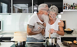 Happy senior couple having fun cooking together at home - Elderly people preparing health lunch in modern kitchen