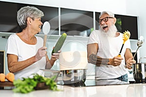 Happy senior couple having fun cooking together at home - Elderly people preparing lunch in modern kitchen