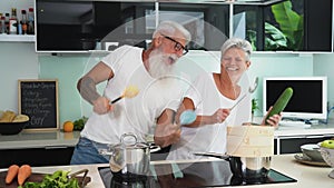 Happy senior couple having fun dancing together at home - Elderly people preparing health lunch in modern kitchen