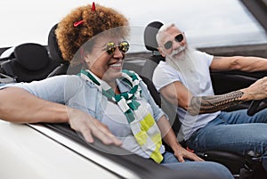 Happy senior couple having fun driving on new convertible car - Mature people enjoying time together during road trip