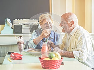 Happy senior couple having fun eating pancakes during united states vacation - Mature people enjoying brunch at bar restaurant -