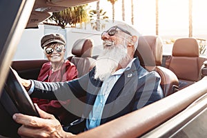 Happy senior couple having fun on new convertible car - Mature people enjoying time together during road trip vacation