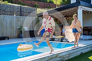 Happy senior couple having fun when walking by swimming pool during summer generation family holidays.