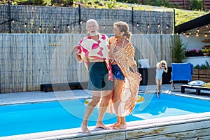 Happy senior couple having fun when walking by swimming pool during summer generation family holidays.