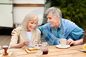 Happy senior couple having toasts with jam and coffee for breakfast at campground