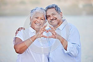 A happy senior couple with a heart sign with their fingers and enjoying fresh nature air on vacation at beach while