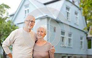Happy senior couple hugging over house background