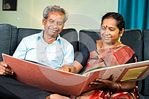 Happy senior couple laughing by looking into to marriage photo album - concept of old memories, nostalgic and family