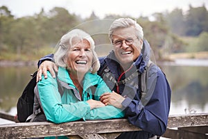 Happy senior couple leaning on a wooden fence laughing to camera, close up, Lake District, UK