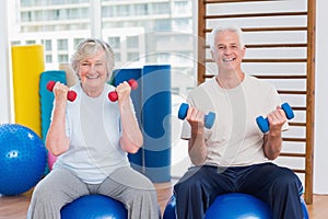 Happy senior couple lifting dumbbells on exercise ball