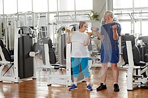 Happy senior couple lifting dumbbells at gym.