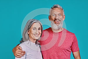 Happy senior couple looking at camera and smiling while standing together against blue background