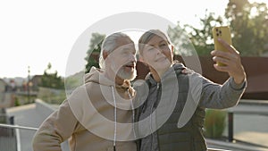 Happy senior couple in love doing selfie standing in the park. Elderly family spending time together, using smartphone
