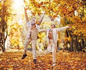 Happy senior couple in love laughing jumping and tossing leaves together in park on autumn day