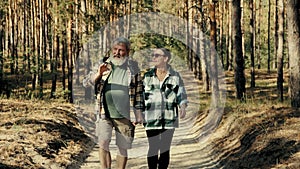 Happy senior couple, man and woman walking in forest on warm sunny day, talking, spending good active time together