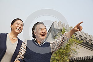 Happy senior couple outdoors pointing by traditional building in Beijing