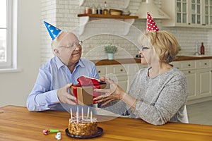 Happy senior couple in party hats celebrating anniversary or wife& x27;s birthday at home