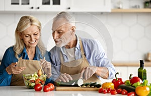 Happy senior couple preparing healthy salad together in kitchen interior