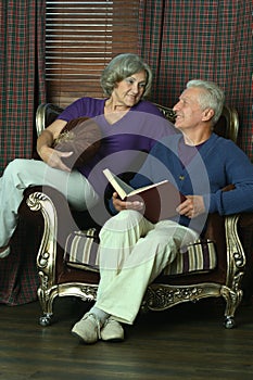 Happy senior couple reading book at home