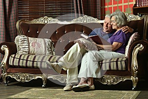 Happy senior couple reading book at home