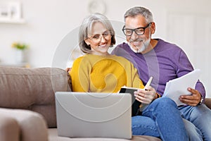 Happy senior couple reading good news in letter while paying bills online on laptop