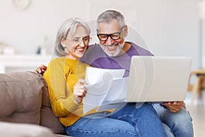 Happy senior couple reading good news in letter while paying bills online on laptop