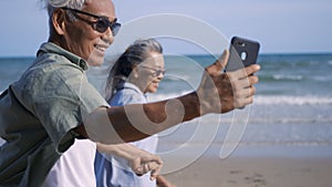 Senior couple relaxing outdoors walking on the sea shore and taking selfie together with smartphone on the beach