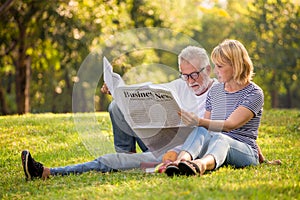 Happy senior couple relaxing in park reading newspaper together . old people sitting on grass in the summer park . Elderly resting