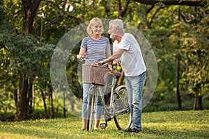 Happy senior couple relaxing at park  walking with bike and talking  together in morning time. old people in the autumn park .
