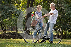 Happy senior couple relaxing at park  walking with bike and talking  together in morning time. old people in the autumn park .