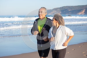 Happy senior couple running along ocean coast on summer day