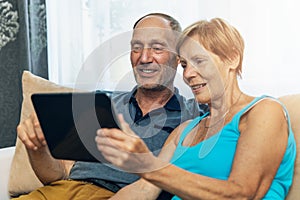 Happy senior couple sitting on couch and using digital tablet