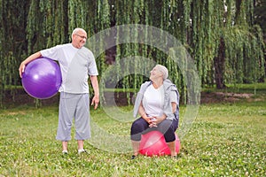 Happy senior couple sitting on fitness balls in park